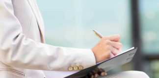Person in beige suit writing on a clipboard