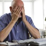 Cognitive Alarm: SHOCKING New Forecast Elderly man sitting at a table with his hands covering his face, surrounded by paperwork