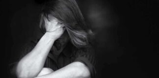 person sitting with knees drawn up and hand over face