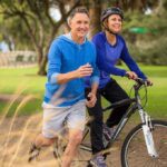 Scientists DISCOVER Aging Secret—Billionaires Race In A couple enjoying outdoor exercise with one riding a bike and the other jogging alongside